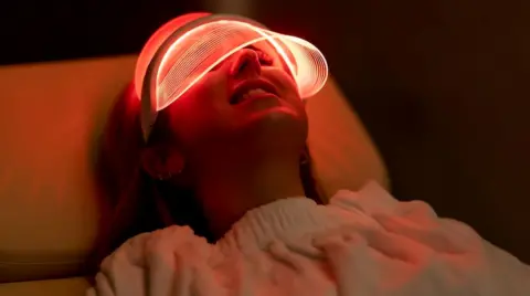 Getty image woman lies with an LED mask that covers her face with a red glow