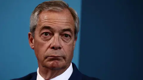 A close up of a man with grey hair and a suit in front of a blue background 