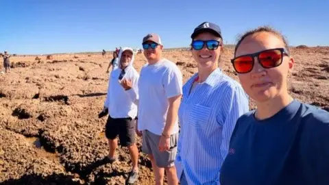 Lara Vafiadis Lara Vafiadis, Dr Susannah Cass, Billy Taylor, and Glyn Roberts take a selfie together while standing on a rocky floor. 