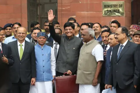 EPA Indian Finance Minister Piyush Goyal (C) holds his briefcase, containing the Union Budget documents, as he poses for photos outside the Ministry of Finance for the Parliament House to present the 2019-20 General Budget in New Delhi, India.