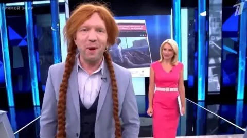 Channel One Russian TV presenter wearing a wig, smiling