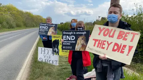 People holding signs by the side of the road.