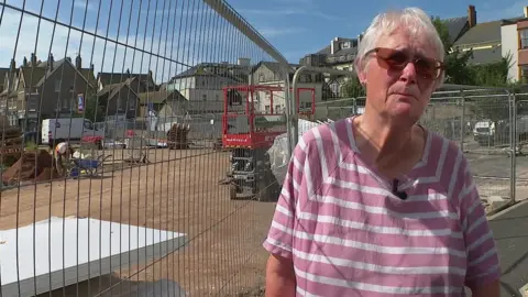 BBC Janet Phillips leaning up against railings at a building site