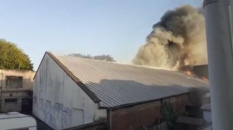 A warehouse with flames and a big plume of smoke