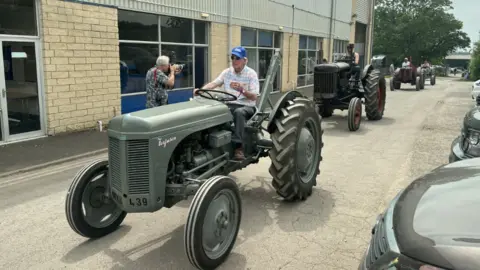 A line of vintage tractors driving down a road at the Bath and West Show.