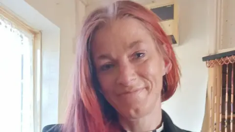 West Midlands Police A headshot of a woman with red hair. She is smiling and standing next to window.