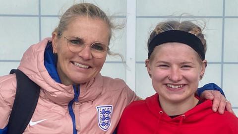 Sarina Wiegman with her arm around Elise Packwood, the pair are both smiling and looking directly at the camera.