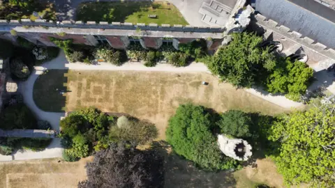 An aerial shot looking down at a lawn outside Bishop's Palace show's symmetrical patterns burnt into the grass. A small square is clearly visible inside a larger square. 
