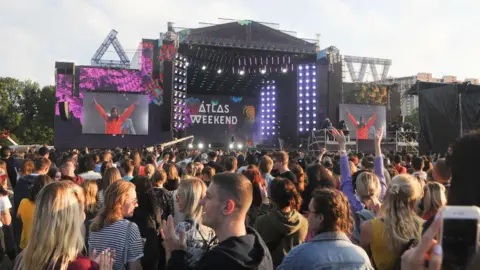 Getty Images A crowd of young people stand in front of a big music stage at a music festival. On the screen behind the stage are the words "Atlas Weekend"