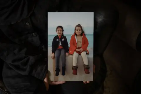 Joel Gunter/BBC Rihab holds a picture of her daughters Tea and Naya on the waterfront in Beirut.