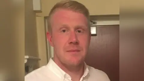 A man wearing a light coloured shirt and a door in the background.
