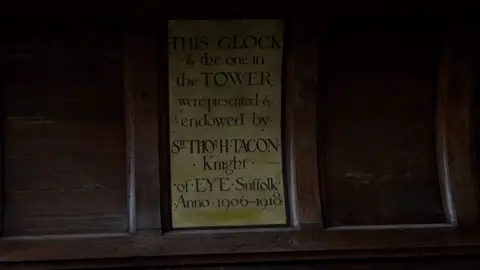 Qays Najm/BBC A sign in a wood panel at County Hall which reads: "This clock and the one by the tower were presented & endowed by Sir Thosh Tacon Knight of Eye Suffolk Anno 1906-1918."