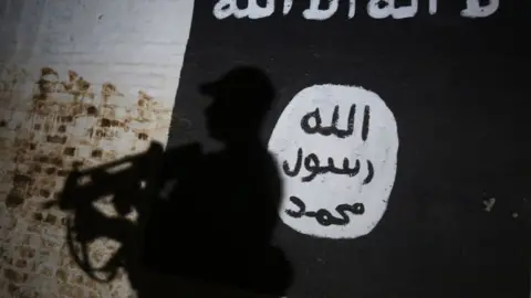 Getty Images The shadow of an Iraqi soldier is cast over the Islamic State flag