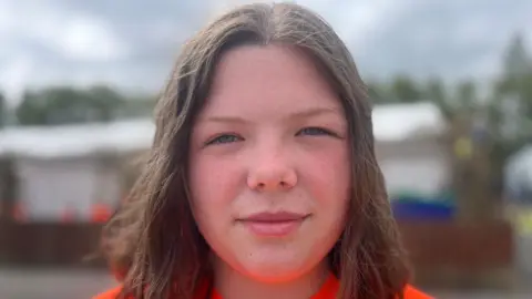 A girl with dark hair wearing an orange top
