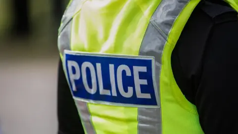 The back of a green fluorescent police vest, with reflective stripes and a blue patch with the word 'police' in grey lettering.  