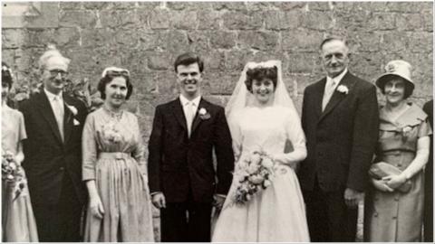 Black and white photo of a bride and groom and their families photographed outside