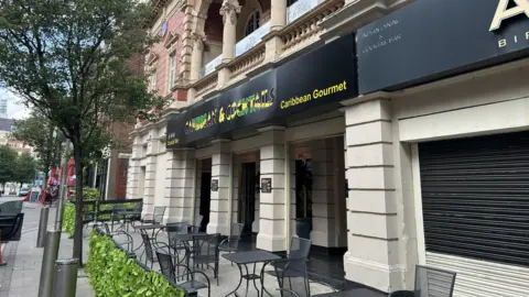 The building today as a Caribbean restaurant. It is an early example of cinema architecture with brick, stone and terracotta dressings. Here, it has a jamaican flag and says Caribbean & Cocktails.