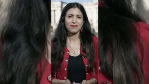BBC Journalist Noon Nanji has long dark hair and is wearing a red jacket over a black top.