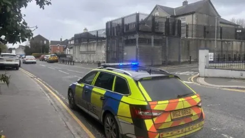 A yellow and blue police car parked outside Strabane police station 