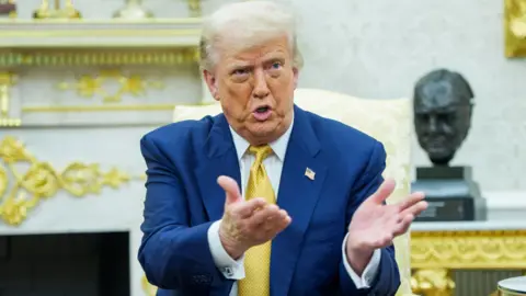 Trump has his hands up wearing a blue suit and yellow tie
