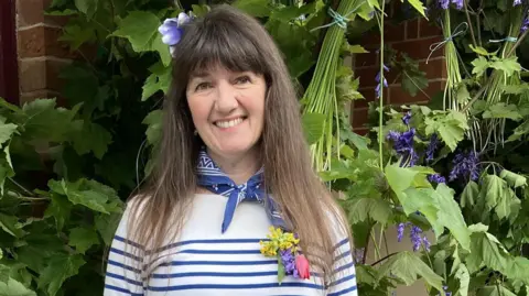 A woman in a blue and white striped top and a blue neckerchief smiles for the camera.