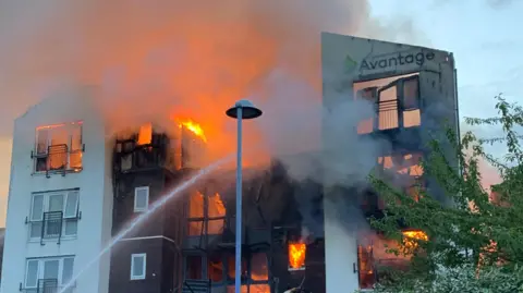 Cheshire Fire & Rescue Service A flat complex on fire. Fire engulfs the building, a large water jet goes into the building trying to extinguish the flames.