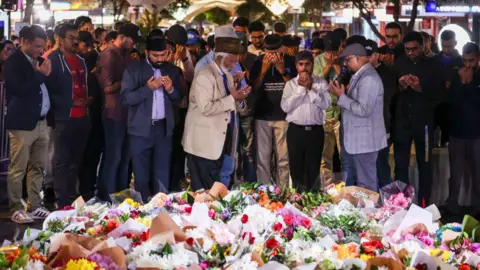 Getty Images Members of the Ahmadiyya Muslim Community of Australia offer prayers in front of flowers left outside the Westfield Bondi Junction shopping mall