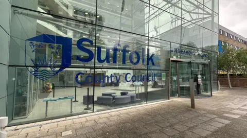 Alice Cunningham/BBC A view of the entrance into Suffolk County Council headquarters. It is a glass building with the council's name and logo painted on the glass in blue.