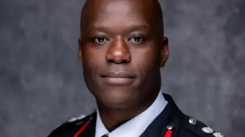 West Midlands Fire Service Wayne Brown's head and shoulders are pictured. He is wearing his fire service uniform in front of a grey background and is looking at the camera.