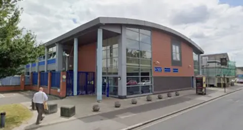 Exterior view of Croydon Police Station and Windmill Road Custody Suite, a modern two-storey building with glass panelling and red-brown cladding.