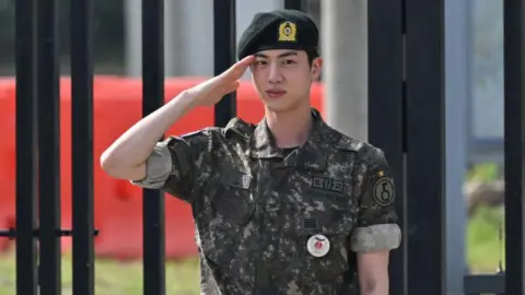 K-pop boy band BTS member Jin salutes after being discharged from his mandatory military service in front of a military base