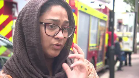 Rida, a woman wearing glasses, a brown head covering and orange dress