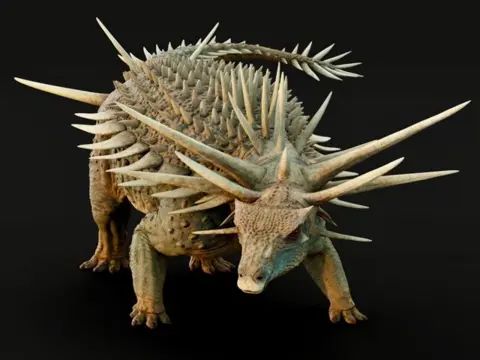 Matt Dempsey The dinosaur has brown green skin against a black background. Its face is like a crocodile with prominent spikes coming out of its neck and the top of its head - with smaller spikes running down its back