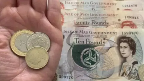 Manx coins in a hand next to Manx bank notes
