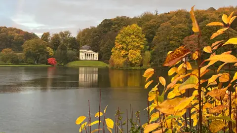 Image shows the National Trust's Stourhead Estate garden with yellowing leaves in the foreground.