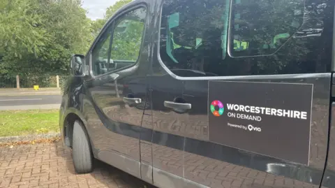 A black mini-bus with a sign reading "Worcestershire on demand" on the side of the vehicle. 
