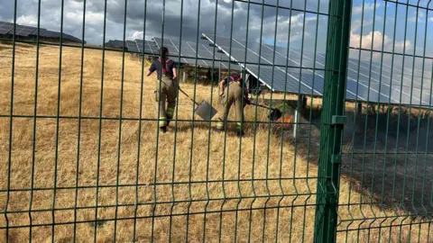 Shirebrook Fire Station Firefighters reach under a solar panel to deal with a fire. 