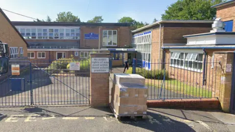 An exterior of a redbrick primary school with blue gates. There is a sign on the gates saying 'no public rights of way exist within these school premises.'