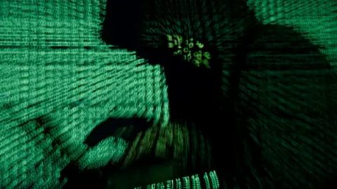 A man holds a laptop computer as green cyber code is projected on him.
