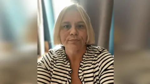 Handout Vicki in a black and white striped top. She has a blonde bob haircut. 