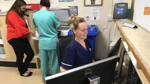 BBC A senior nurse at reception deciding whether to send patients to A&E or urgent care centre next door