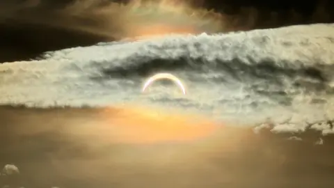 BBC Weather Watchers/Bettys Mum The partial solar eclipse captured in Redcar. The dusky sky is covered in clouds and a slither of sun is visible.