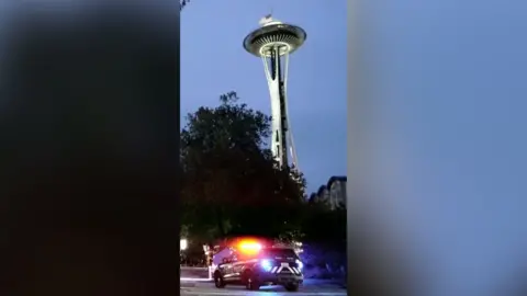The Seattle space needle in the evening sky. There is a police car in the foreground.