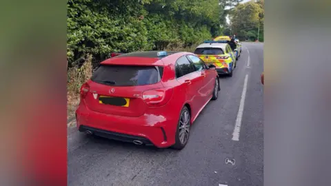 TVP A red car parked behind two police cars on a road.