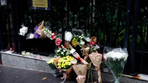 Getty Images A photograph shows bunches of flowers displayed outside the building in Paris on October 17, 2022, where lived a 12-year-old schoolgirl, named Lola, three days after her body was discovered in a trunk in the 19th district. - A woman and a man are presented to an examining magistrate on October 17, 2022 in Paris with a view to an indictment for murder and rape with acts of torture and barbarism