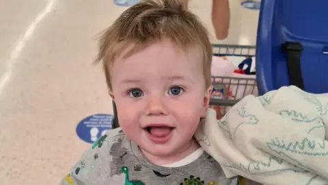 Family photo Oliver Steeper smiling at the camera sat in a supermarket trolley