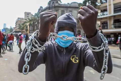 BONIFACE MUTHONI/GETTY IMAGES A protester with both hands tied with a chain takes part in an anti-government protest on 2 July.