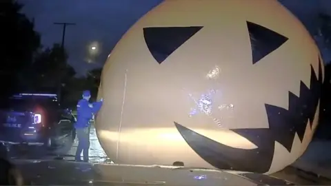 Large inflatable pumpkin on road, police officer pushing it out of the way