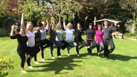 Yorkshire Centre for Wellbeing Eleven people stand in a garden doing yoga poses.