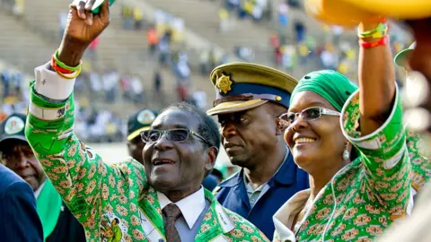 Robert Mugabe (L) and his wife Grace Mugabe (R) - both dressed in matching Zanu-PF regalia - greet supporters at a rally in Harare - July 2013. 